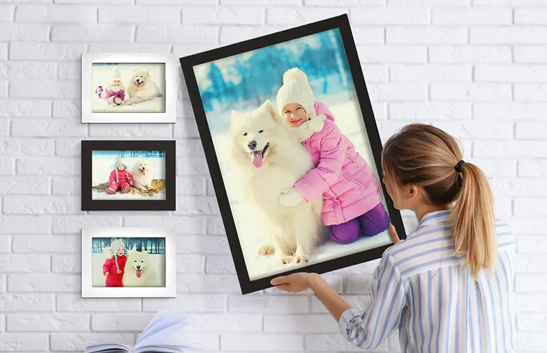 Cadre photo personnalisé : une femme accroche un grand tirage photo d’enfant et son chien Samoyède, entouré de photos plus petites.